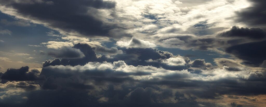 Photo d'un ciel nuageux avec du soleil et des nuages sombres.