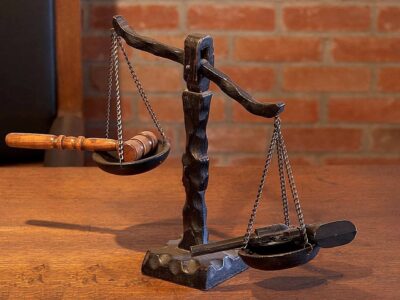 Photo of a scale with a revolver in one pan and the hammer of justice in the other pan.